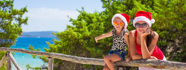 Młoda matka i mała dziewczynka w czerwonym kapeluszu Boże Narodzenie na tropikalnej plaży — Zdjęcie stockowe
