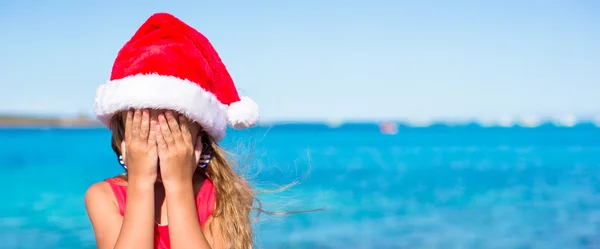 Little girl in christmas hat covering her face background the sea — Stock Photo, Image