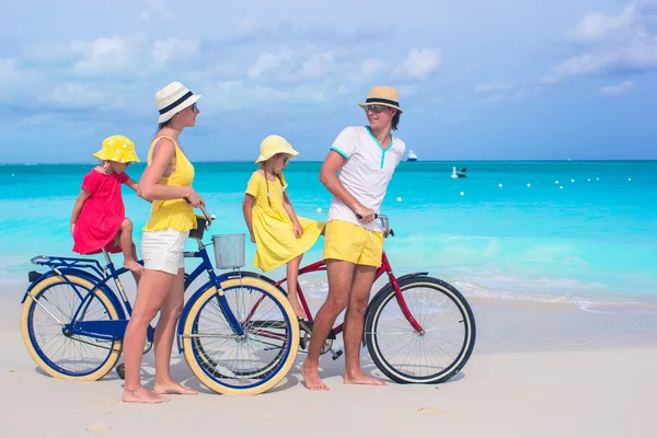 Young happy family riding bicycles on tropical beach — Stock Photo, Image