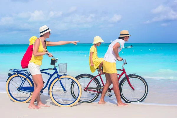 Young happy family riding bicycles on tropical beach — Stock Photo, Image