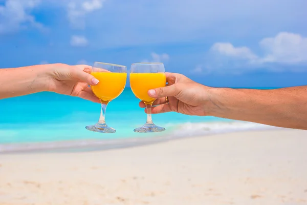 Dos manos sostienen vasos con zumo de naranja fondo cielo azul — Foto de Stock