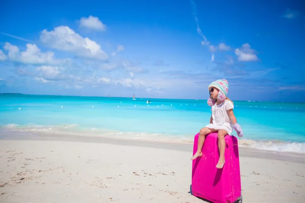 Adorable girl in warm winter hat and mittens walking with luggage on beach — Stock Photo, Image
