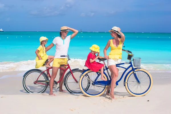 Young family of four riding bicycles on tropical sand beach — Stock Photo, Image