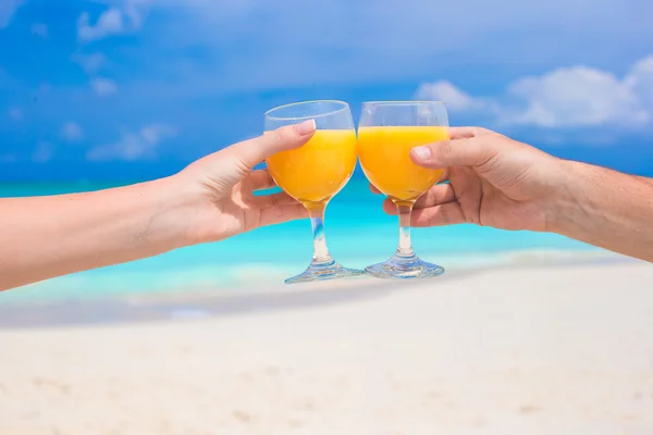 Dos manos sostienen vasos con zumo de naranja fondo cielo azul — Foto de Stock