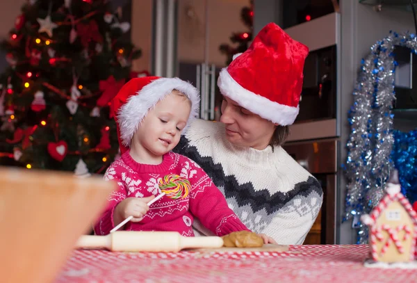 若いお父さんとサンタ帽子の小さな娘クリスマスのジンジャーブレッド クッキーを焼く — ストック写真