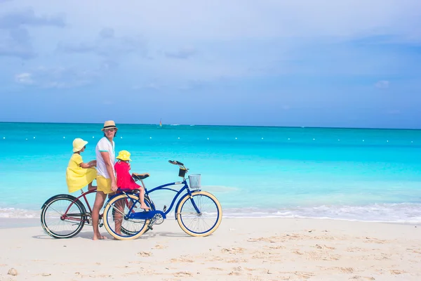 Happy dad and cute girls riding bicycles on tropical beach — Stock Photo, Image