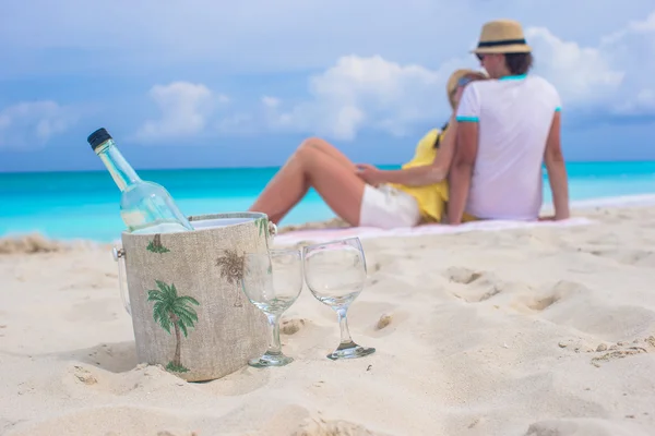 Botella de vino blanco y dos copas fondo feliz pareja en la playa de arena —  Fotos de Stock