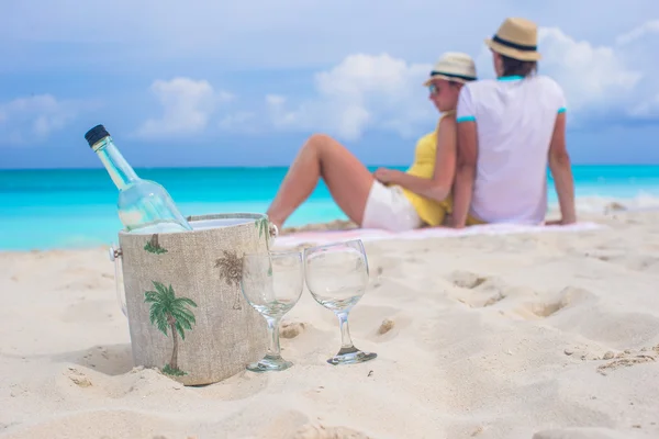 Botella de vino blanco y dos copas fondo feliz pareja en la playa de arena —  Fotos de Stock