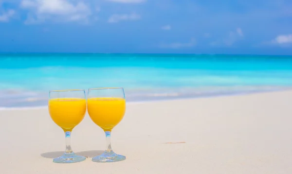 Primo piano di due bicchieri di succo d'arancia sulla spiaggia tropicale bianca — Foto Stock