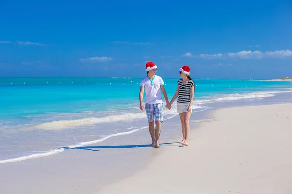 Junges glückliches Paar in roten Weihnachtsmützen am tropischen Strand — Stockfoto