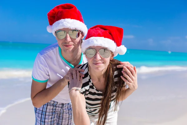 Portret van een jong koppel in santa hoeden genieten van strandvakantie — Stockfoto