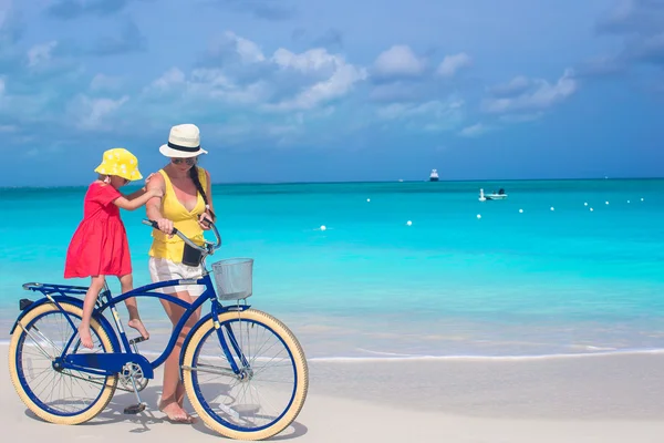 Happy mom and cute girl riding bicycles on tropical beach — Stock Photo, Image