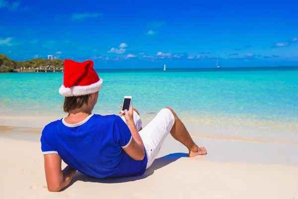 Jovem em santa chapéu falando ao telefone na praia tropical — Fotografia de Stock