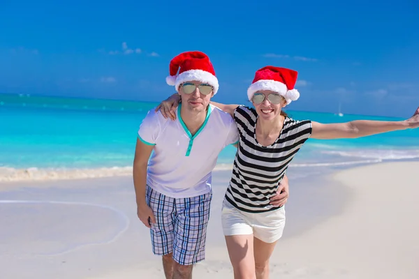 Portret van een jong koppel in santa hoeden genieten van strandvakantie — Stockfoto