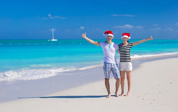 Junges glückliches Paar in roten Weihnachtsmützen am tropischen Strand — Stockfoto