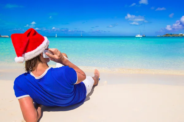 Young man in santa hat talking on phone at tropical beach — Stock Photo, Image