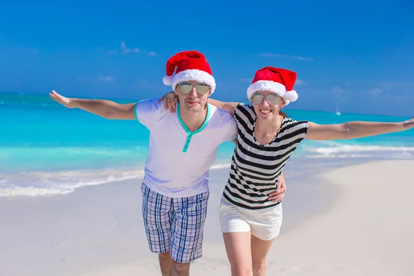 Portret van een jong koppel in santa hoeden genieten van strandvakantie — Stockfoto