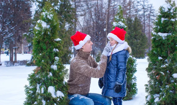 Adorable petite fille et papa heureux dans chapeaux de Père Noël à l'extérieur — Photo