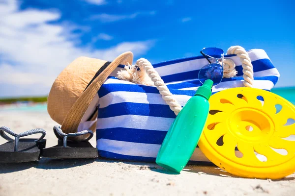 Stripe bag, straw hat, sunblock and towel on beach — Stock Photo, Image