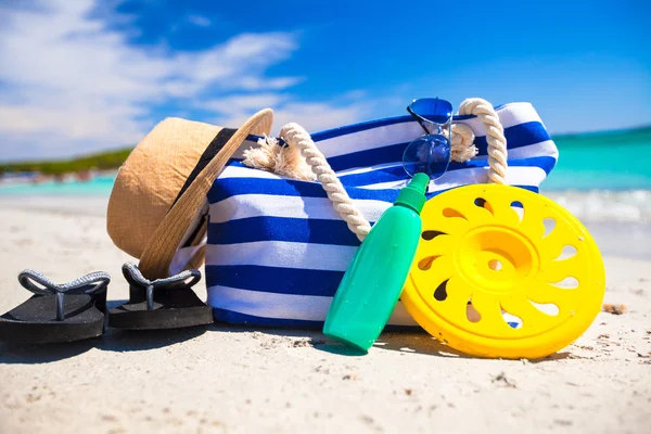 Stripe bag, straw hat, sunblock and towel on beach — Stock Photo, Image