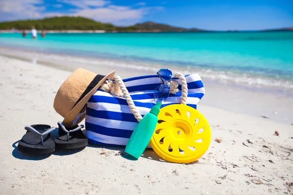 Borsa a righe, cappello di paglia, crema solare e asciugamano sulla spiaggia tropicale bianca — Foto Stock