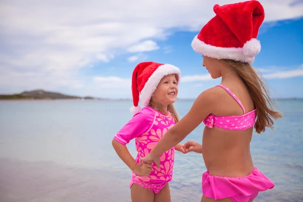 Kleine entzückende Mädchen in Weihnachtsmützen während des Strandurlaubs — Stockfoto