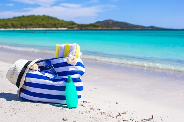 Borsa a righe, cappello di paglia, crema solare e asciugamano sulla spiaggia — Foto Stock