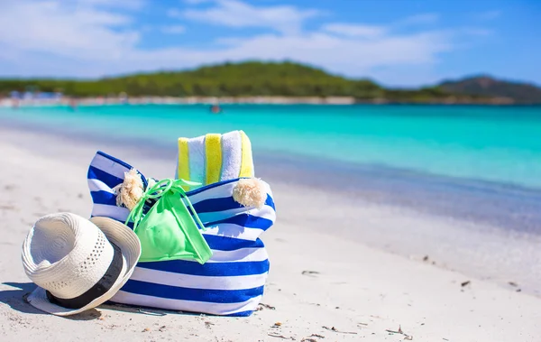 Sac à rayures, chapeau de paille, crème solaire et serviette sur la plage — Photo