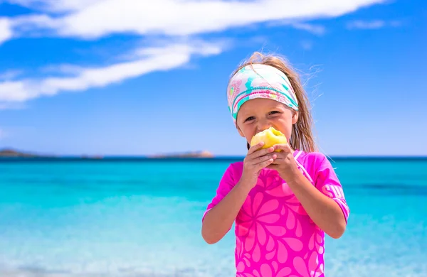 Urocze dziewczynki jeść jabłko na tropikalnej plaży podczas wakacji — Zdjęcie stockowe