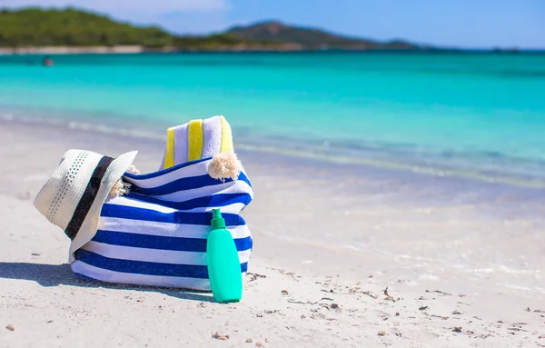 Stripe bag, straw hat, sunblock and towel on beach — Stock Photo, Image