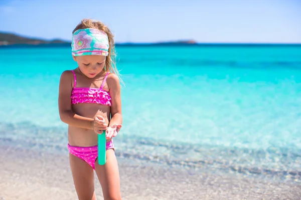 Piccola adorabile ragazza in costume da bagno con bottiglia di crema abbronzante — Foto Stock