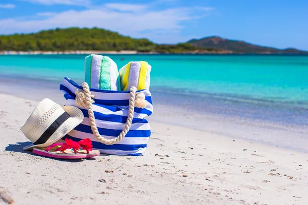 Blå taske, halmhat, klipklapper og håndklæde på hvid strand - Stock-foto