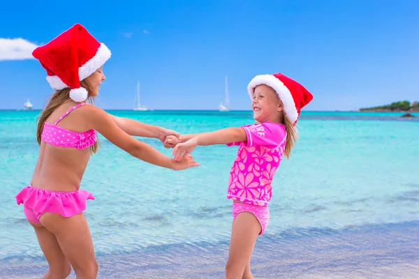 Kleine entzückende Mädchen in Weihnachtsmützen während des Strandurlaubs — Stockfoto