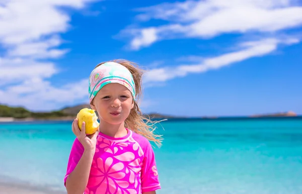 Entzückendes kleines Mädchen isst im Urlaub Apfel am tropischen Strand — Stockfoto