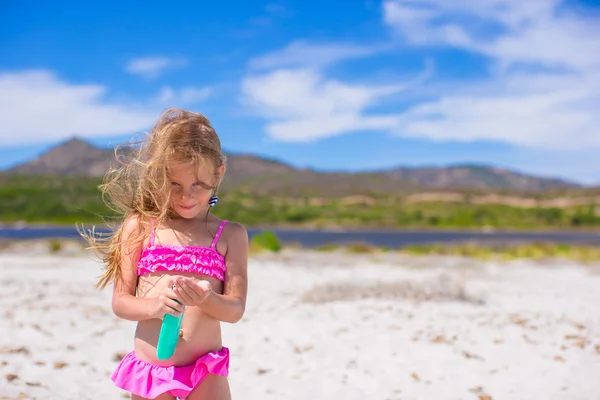 Piccola adorabile ragazza in costume da bagno con bottiglia di crema abbronzante — Foto Stock