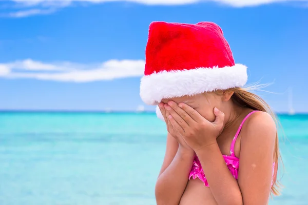 Schattig meisje in rode kerstmuts op tropisch strand — Stockfoto