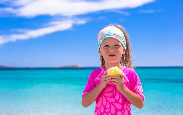 Bedårande liten flicka äter äpple på tropical beach under semester — Stockfoto