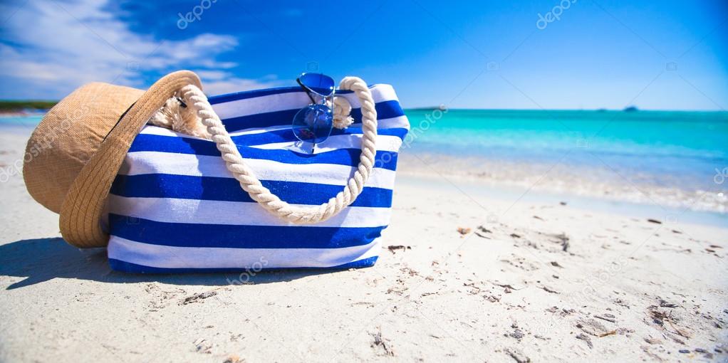 Stripe bag, straw hat, sunblock and towel on white tropical beach