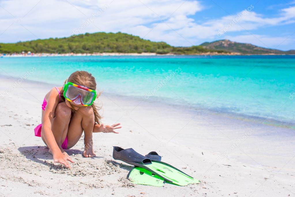 Little girl with flippers and goggles for snorkling on white beach