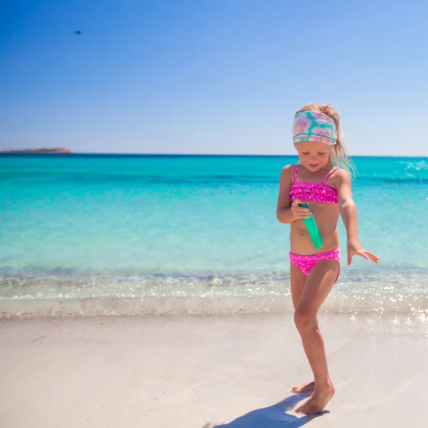 Piccola adorabile ragazza in costume da bagno con bottiglia di crema abbronzante — Foto Stock