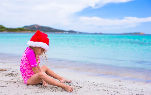 Kleines entzückendes Mädchen mit rotem Weihnachtsmann-Hut am tropischen Strand — Stockfoto