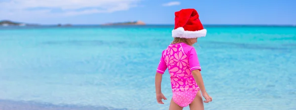 Kleines entzückendes Mädchen mit rotem Weihnachtsmann-Hut am tropischen Strand — Stockfoto