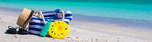 Stripe bag, straw hat, sunblock and towel on beach — Stock Photo, Image