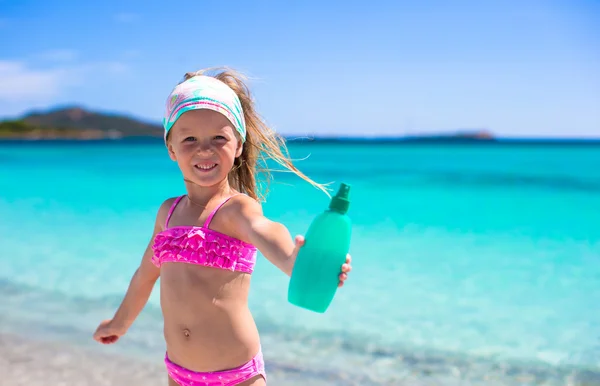 Маленькая очаровательная девочка в купальнике с бутылкой лосьона для загара — стоковое фото