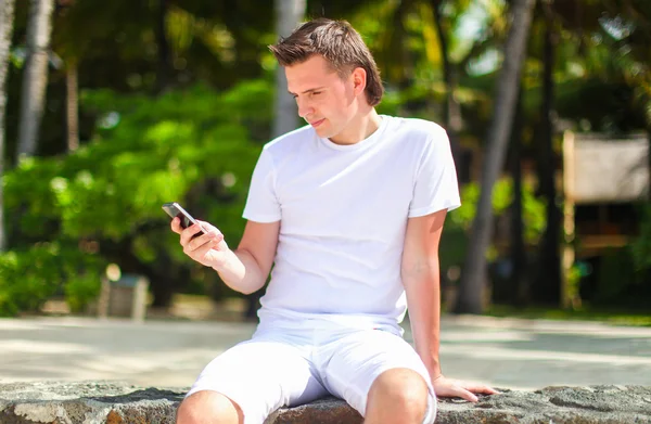 Young man talking on phone during tropical beach vacation — Stock Photo, Image