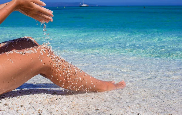 Närbild av kvinnliga ben med småsten bakgrund av det turkosa havet — Stockfoto