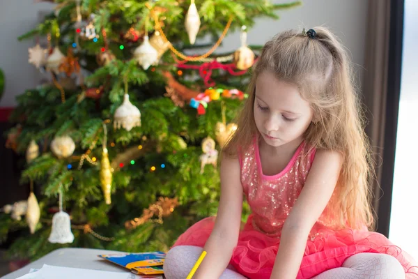 Adorable little girl drawing near Christmas tree — Stock Photo, Image