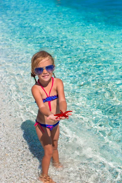 Kleines entzückendes Mädchen mit Seestern am tropischen Strand — Stockfoto