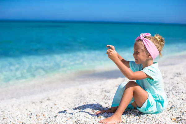 Piccola ragazza carina scattare foto al telefono sulla spiaggia tropicale — Foto Stock