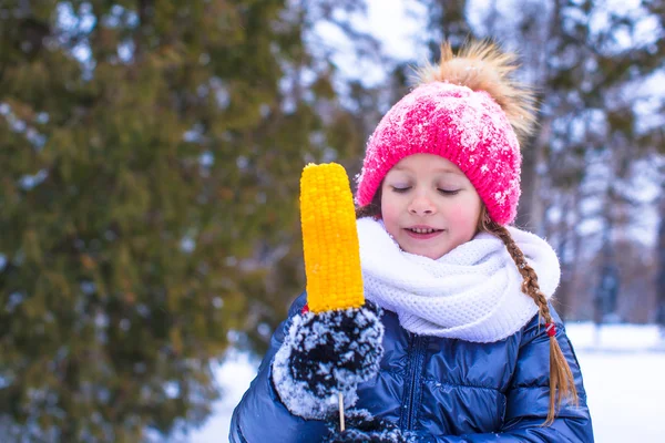 Liten bedårande flicka med majs på vinter park — Stockfoto